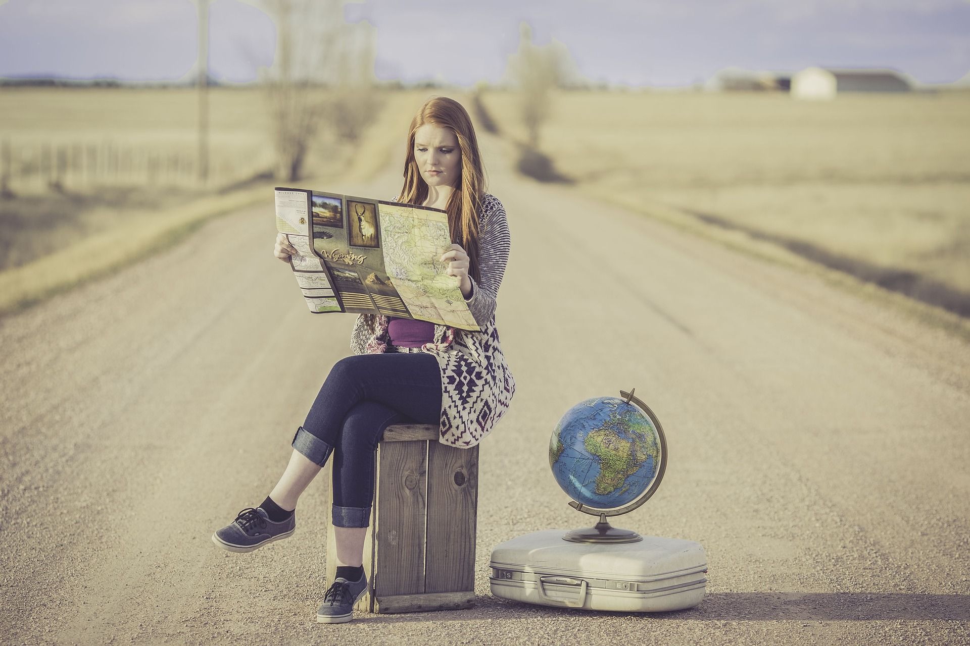 Person sitting on some luggage in the road reading a map